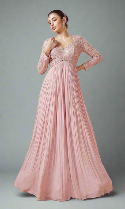 Woman wearing a pink evening gown with floral details in a softly lit room.